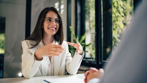 Bankgespräch Eine Frau sitzt gegenüber einer anderen Person an einem Schreibtisch und spricht