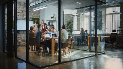 Neugründung In einem Büro sitzt ein Team am Tisch und freut sich über den eigenen Erfolg.
