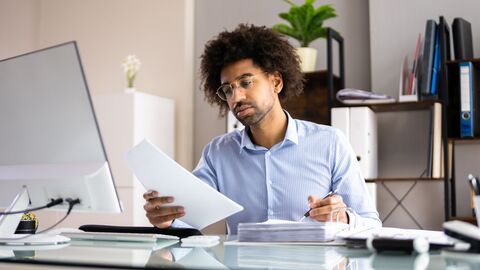Ein Mann sitzt an seinem Schreibtisch und schaut sich seine Unterlagen an