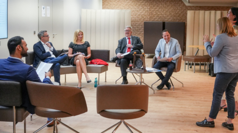 Pitch Arena Eine Gruppe von Personen sitzen in einem Stuhlkreis und hören einer Frau zu, die einen Vortrag hält.