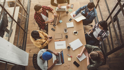 Social Entrepreneurship Von oben ist eine Gruppe von Personen zu sehen, die an einem großen Tisch sitzen und miteinander sprechen.