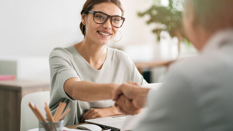Frau gibt andere Person die Hand am Schreibtisch